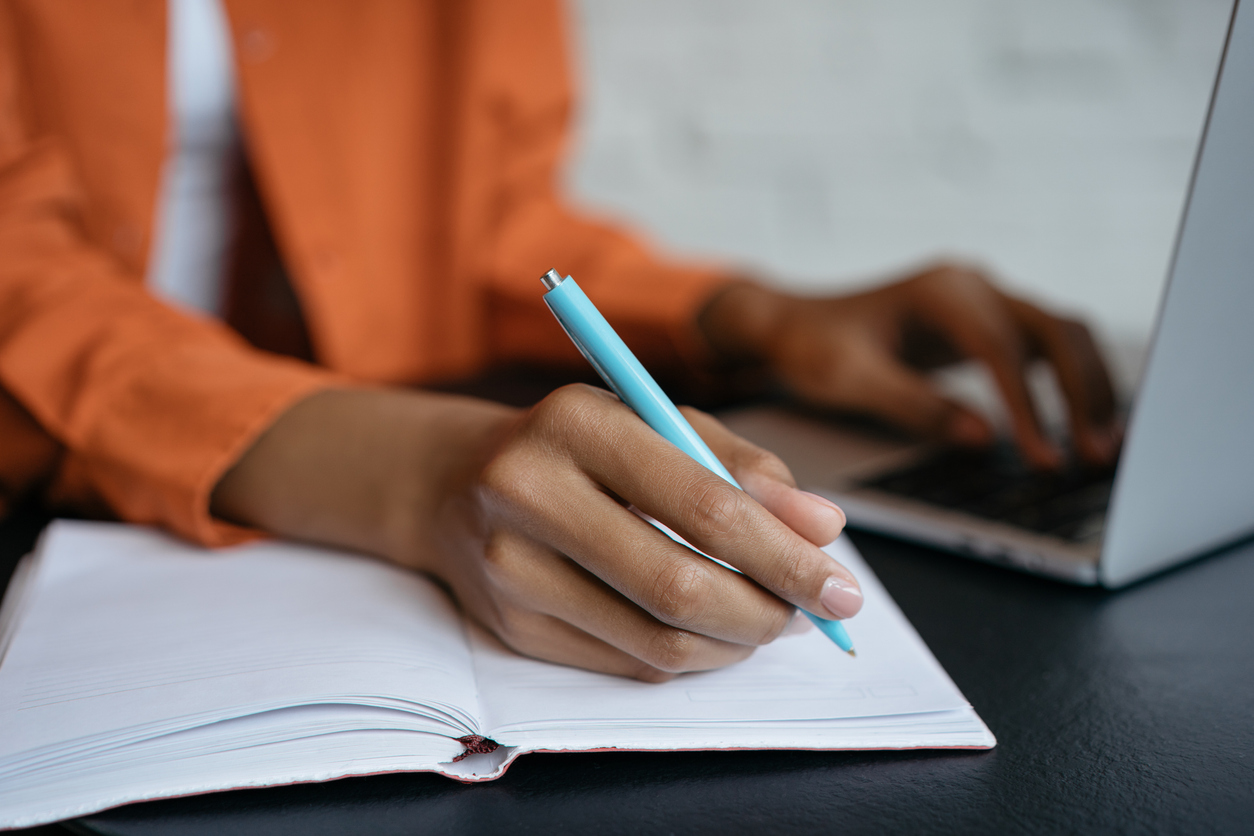 Close-up shot of hand holding pen and writing in noteboo